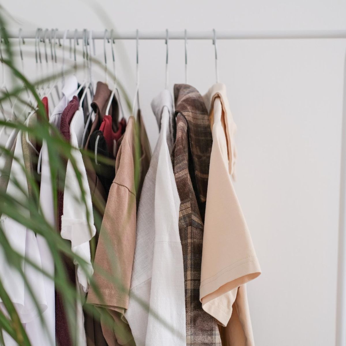 Clothing rack with neatly hung neutral-toned shirts and jackets on white hangers, arranged for an organized seasonal wardrobe rotation.