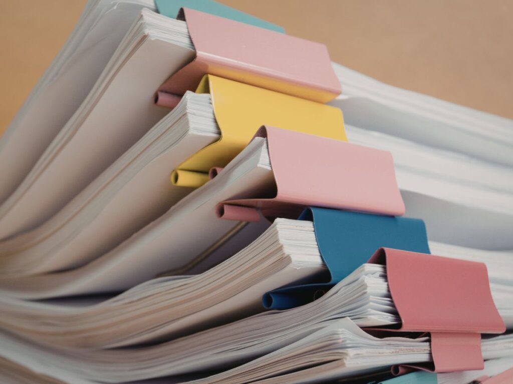 Stack of documents clipped with colorful binder clips in pink, yellow, and blue.