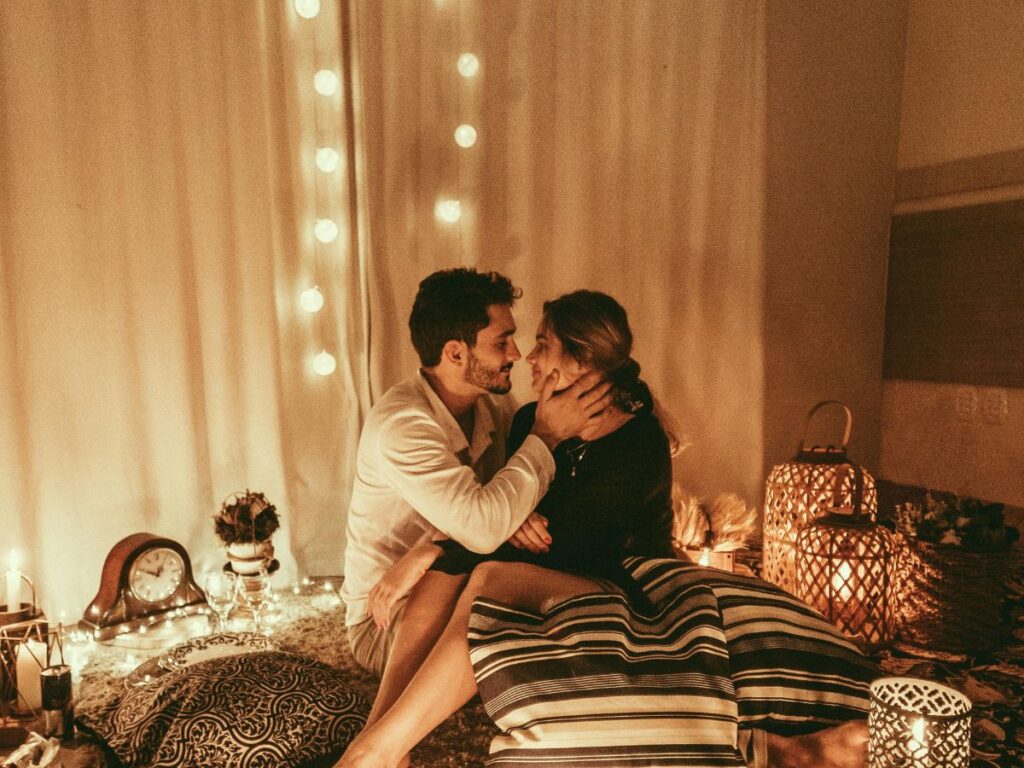 A couple sitting close together in a softly lit room with candles and string lights, sharing an intimate moment.