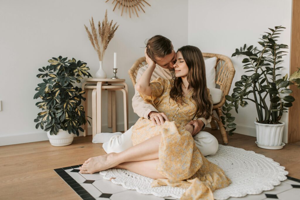 Couple sitting on the floor at home, cuddling in a cozy living room surrounded by plants.