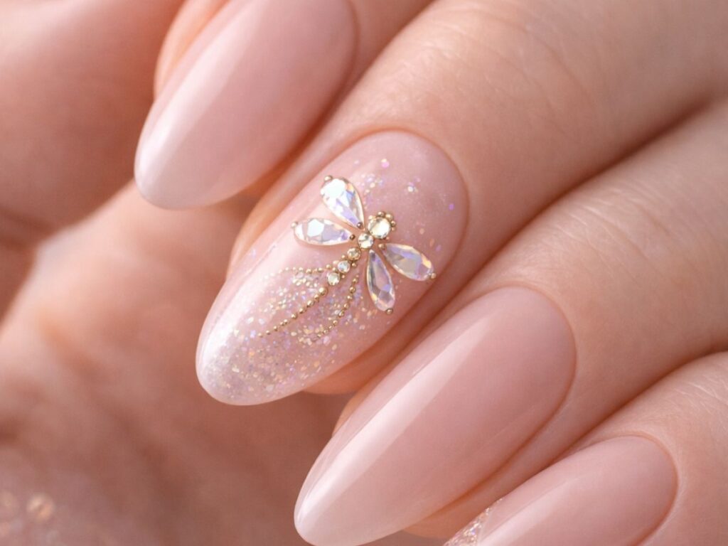 Macro close-up of soft nude almond-shaped nails with subtle glitter accents and a delicate crystal dragonfly design on one nail, glowing under soft natural light.