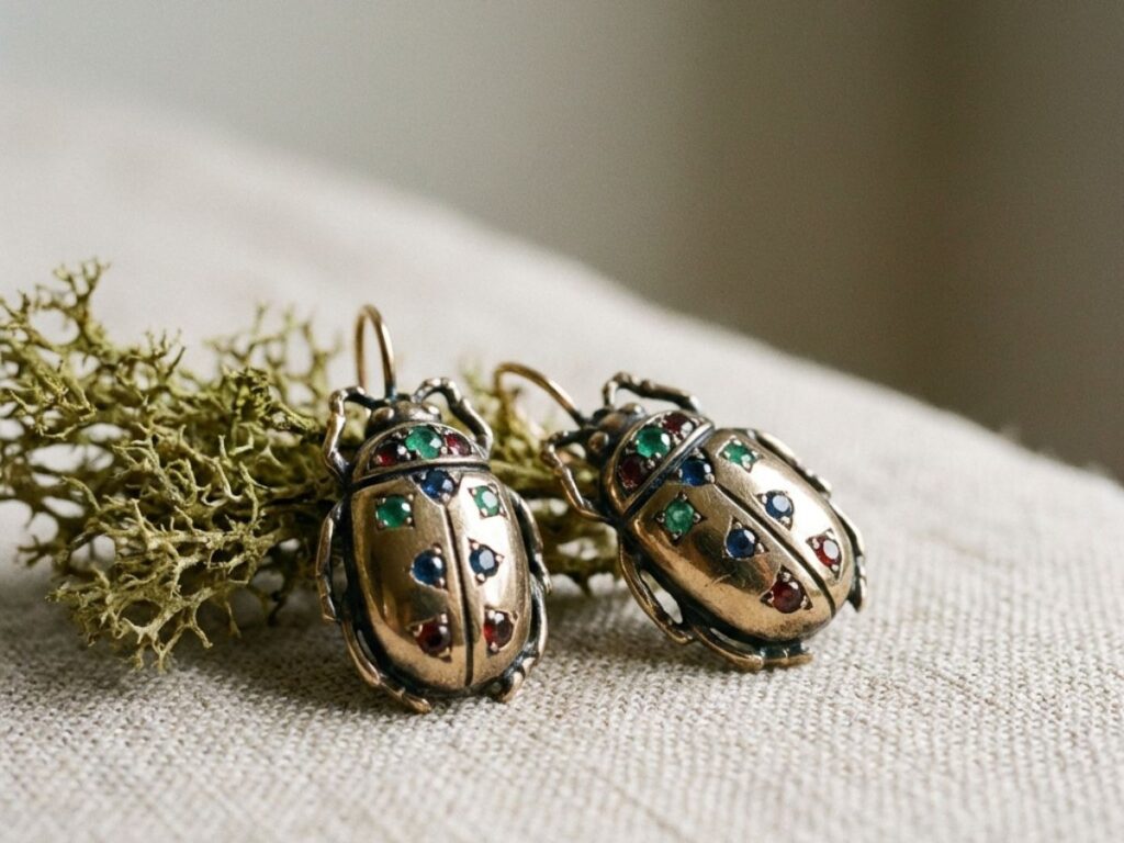 Beetle-shaped earrings with gemstones on neutral fabric