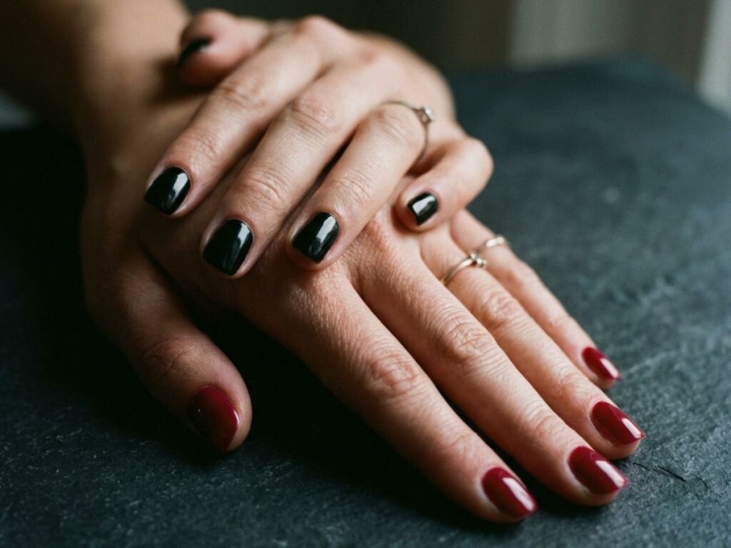 Hands with black and deep red mismatch nails, moody lighting, elegant minimal aesthetic