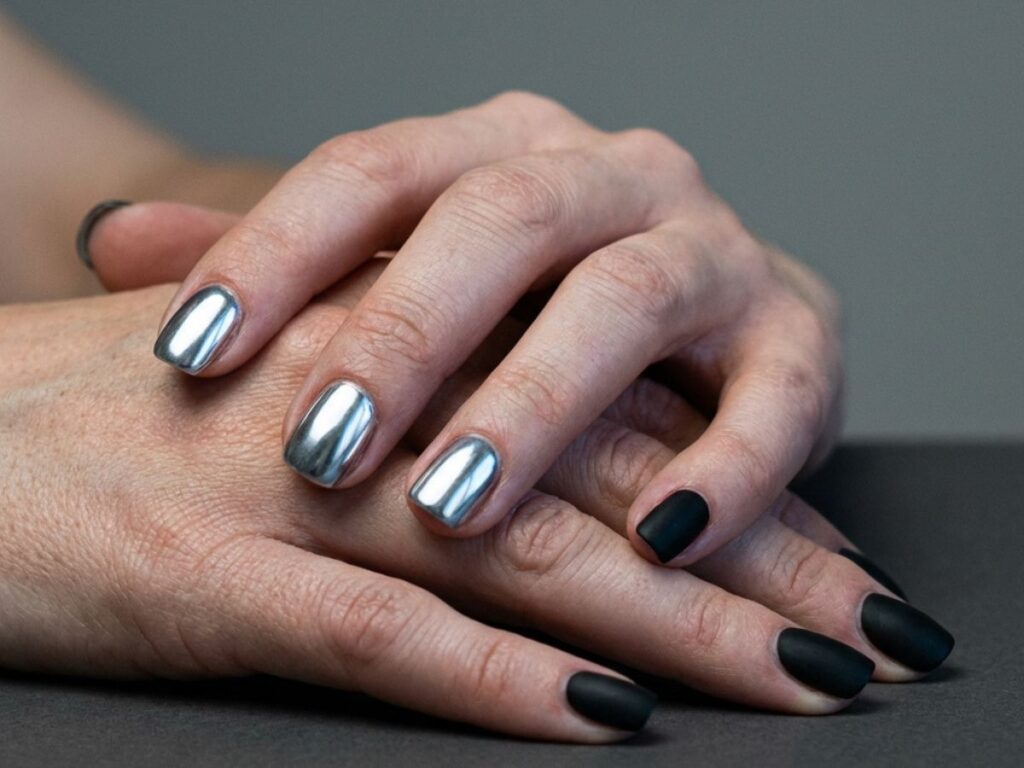Hands with chrome silver and matte black mismatch nails, modern edgy manicure, dark minimal background close-up