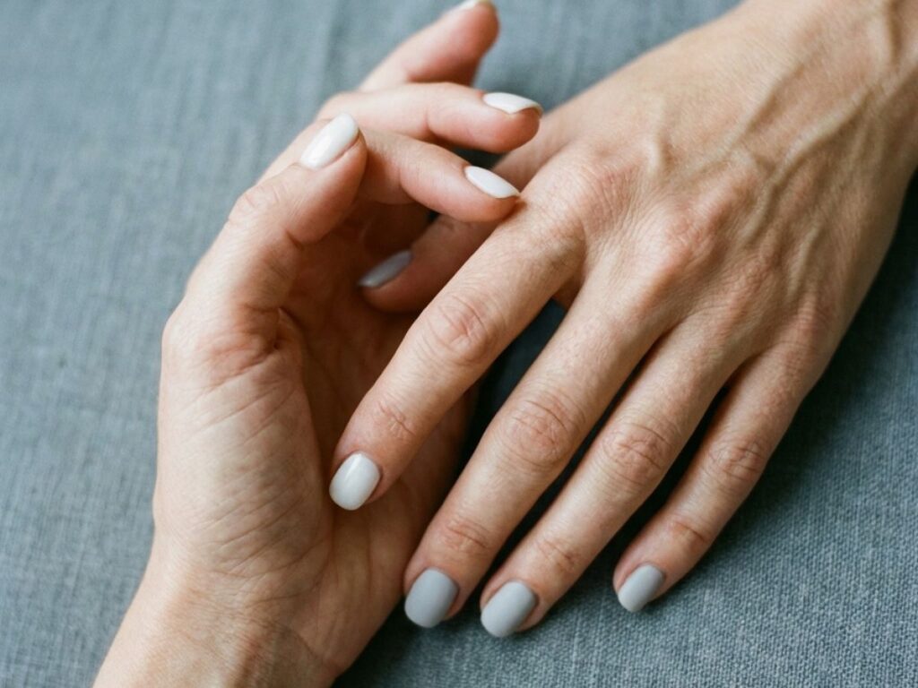 Hands with neutral mismatch manicure featuring white and soft grey nails, minimal aesthetic, natural lighting close-up
