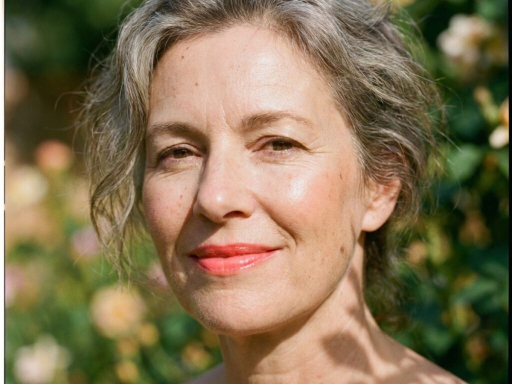 Mature woman outdoors with radiant skin and coral lipstick in sunlight