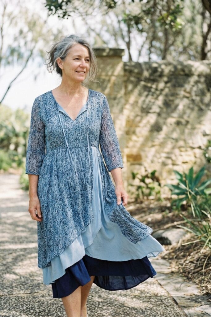 Older woman in a layered blue patterned dress walking along a peaceful garden pathway.
