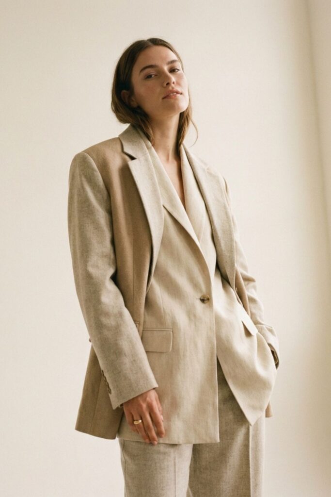 Woman in beige oversized suit posing near window in soft light.