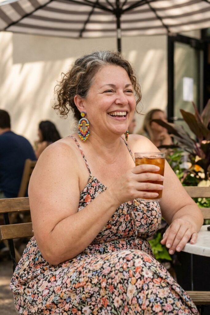 Plus size woman in floral dress laughing with drink at outdoor café