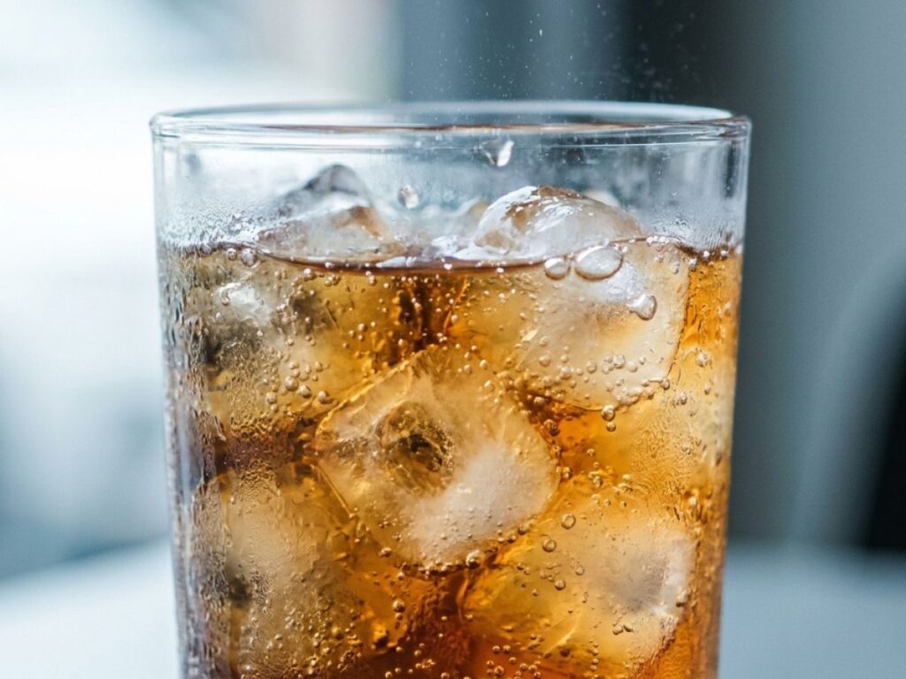 Soda in glass with ice and fizz bubbles close up