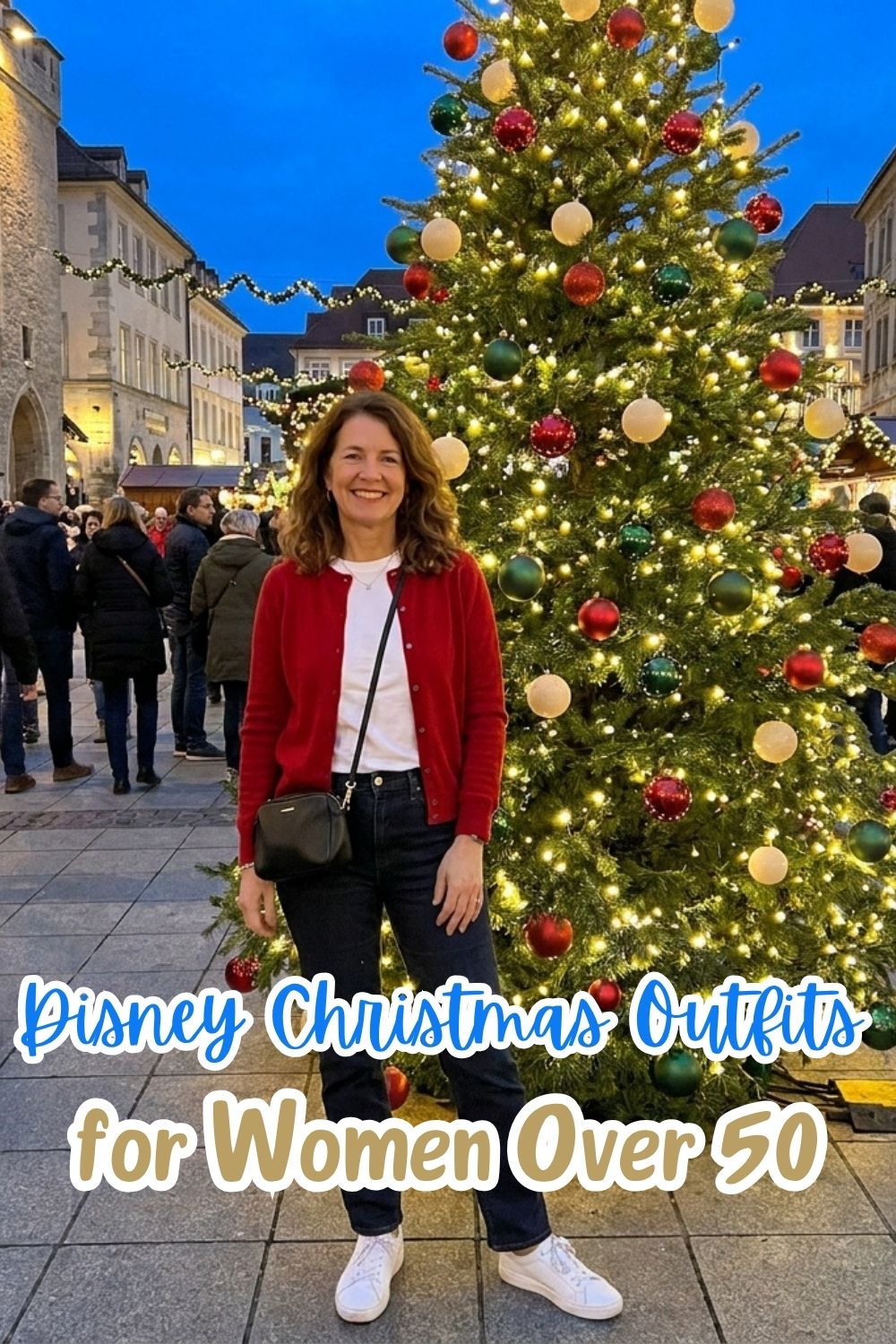 A woman in a red cardigan, white tee, and dark jeans smiles beside a lit Christmas tree, with the text Disney Christmas Outfits for Women Over 50.