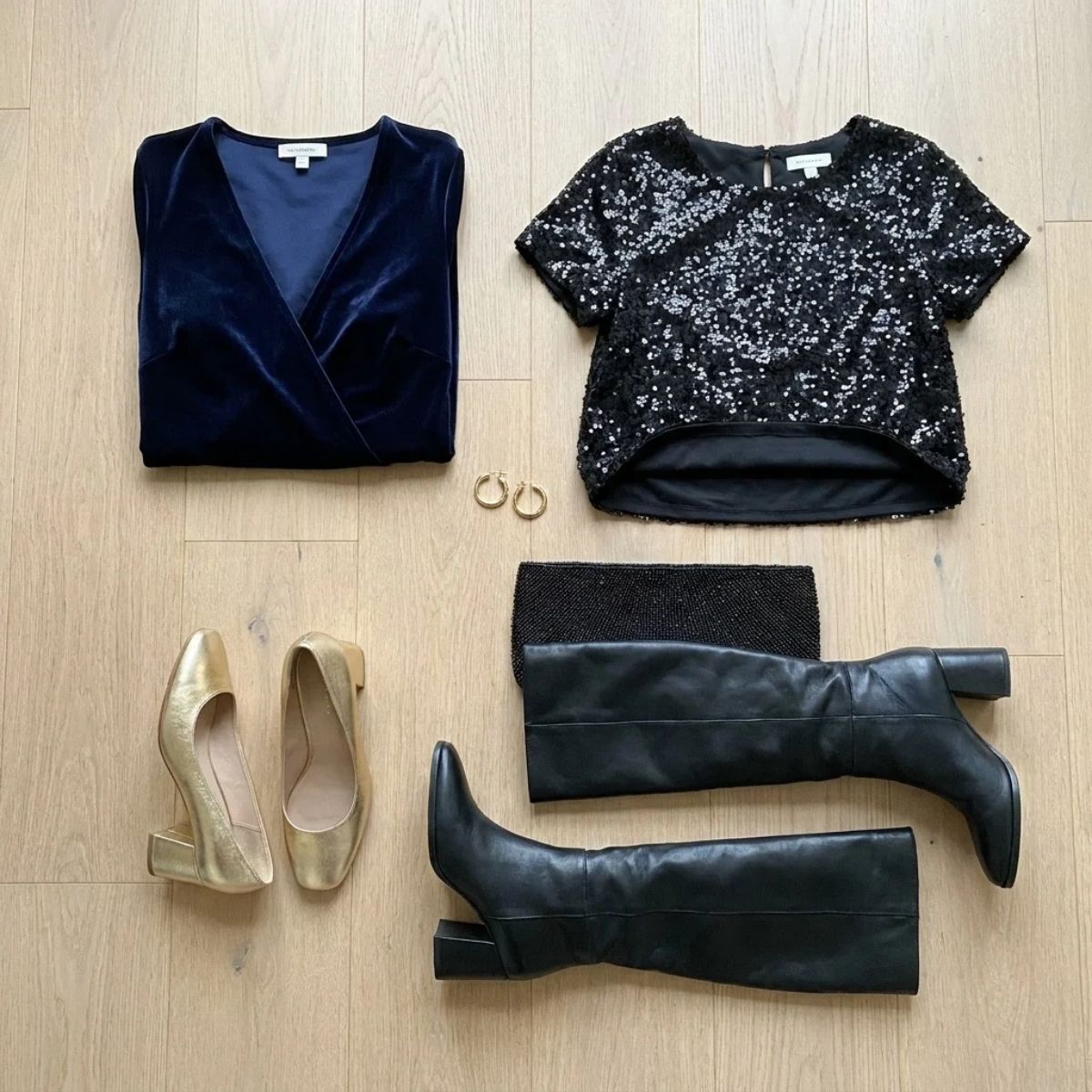 A flat lay of a velvet wrap dress, a lined sequin top turned to show its lining, gold block heels and black wide-calf knee boots on a wooden floor.